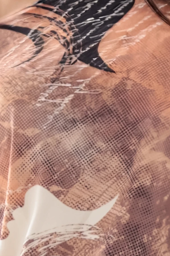 Modelka prezentuje sukienkę z elastycznego materiału w odcieniach brązu z artystycznym nadrukiem i dekoltem, marki Numoco – produkt polski.