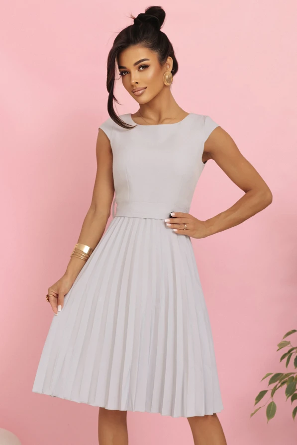 Modelka w eleganckiej plisowanej sukience midi marki Numoco w kolorze jasnoszarym, z krótkim rękawkiem i wiązaniem w talii, prezentująca kreację idealną na wesele, komunię i inne uroczystości.