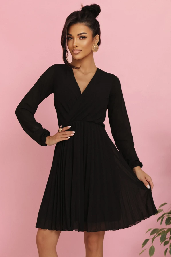 Modelka prezentuje elegancką czarną szyfonową sukienkę marki Numoco z długim rękawem, kopertowym dekoltem i plisowanym dołem – idealną na wieczór, wesele lub specjalne okazje. Produkt polski, sfotografowany na różowym tle.