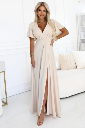 Modelka w eleganckiej beżowej sukience maxi z dekoltem i rozcięciem na nodze – kreacja od polskiego producenta Numoco, idealna na wesele lub wyjątkowe okazje.}