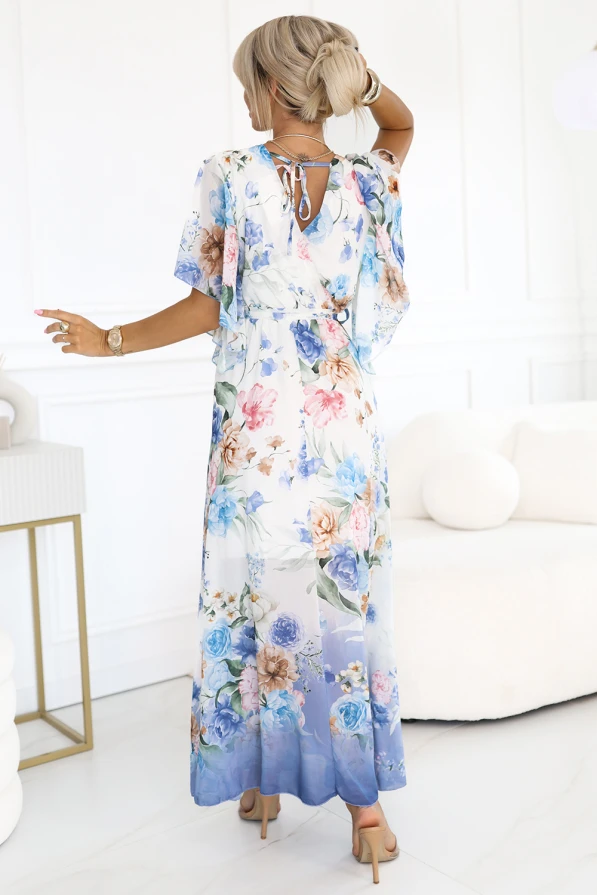 Modelka prezentuje romantyczną, kwiatową sukienkę maxi z przewiewnego szyfonu, ozdobioną pastelowym wzorem w odcieniach niebieskiego. Stylizacja podkreśla kobiecą sylwetkę i idealnie wpisuje się w letni klimat eleganckich przyjęć i spacerów.