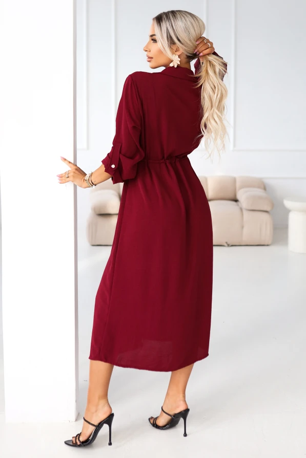 Elegancka stylizacja: modelka prezentuje bordową sukienkę midi typu shirt dress z kieszeniami na piersi, w jasnym wnętrzu glamour.